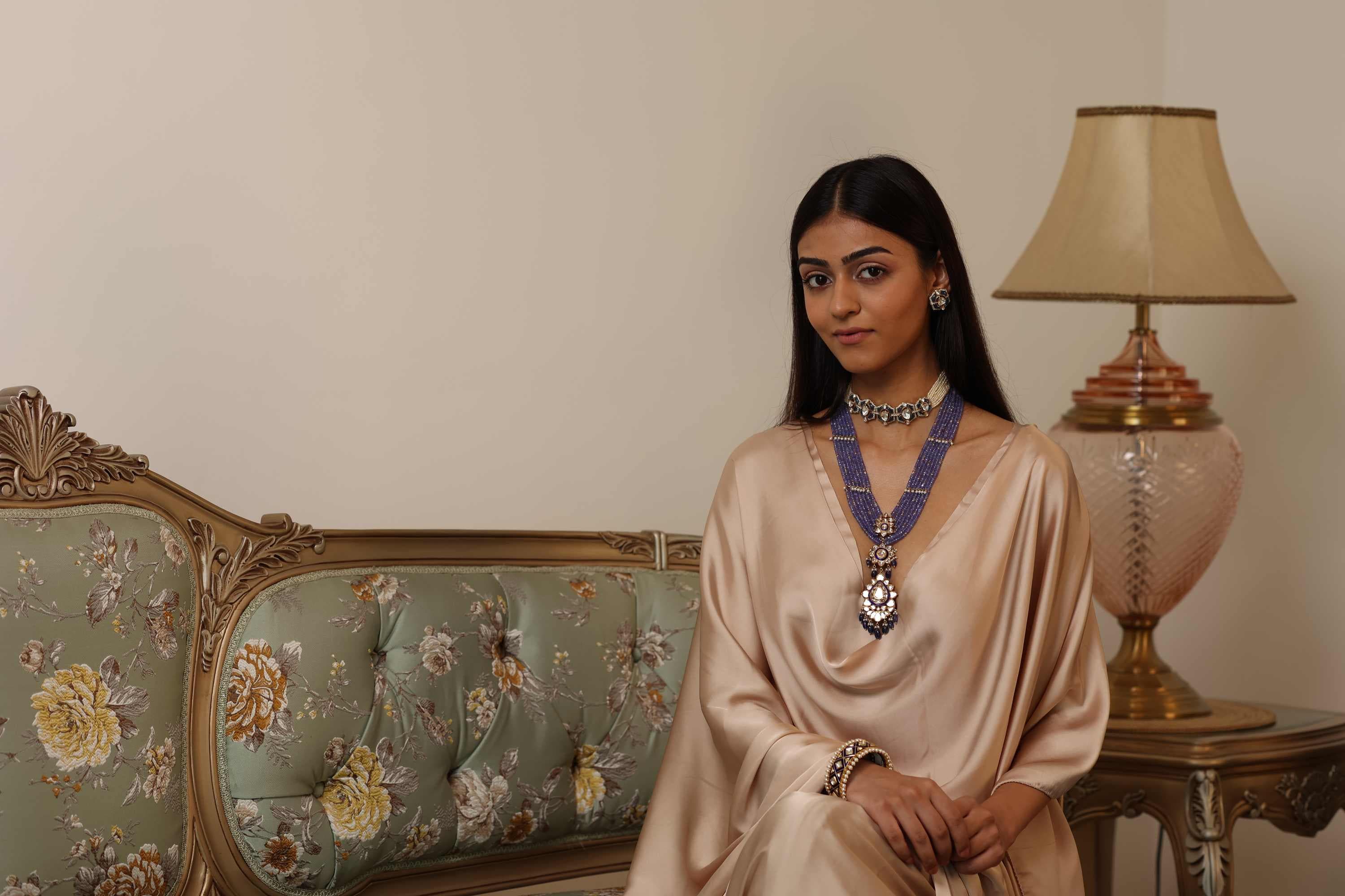A model in a beige kaftan and polki necklace on a carved settee