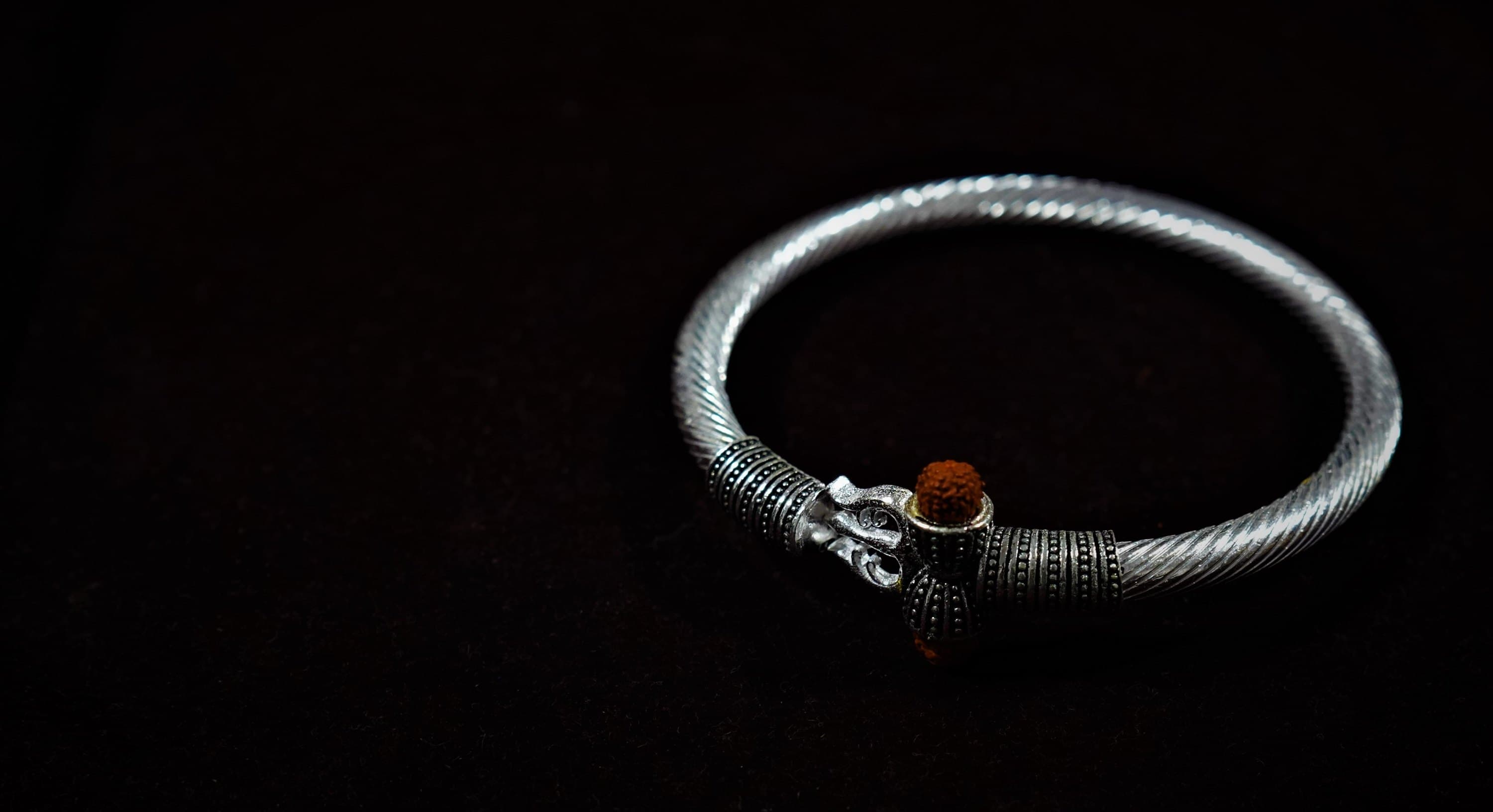 A silver bangle set with rudraksha, lit on black