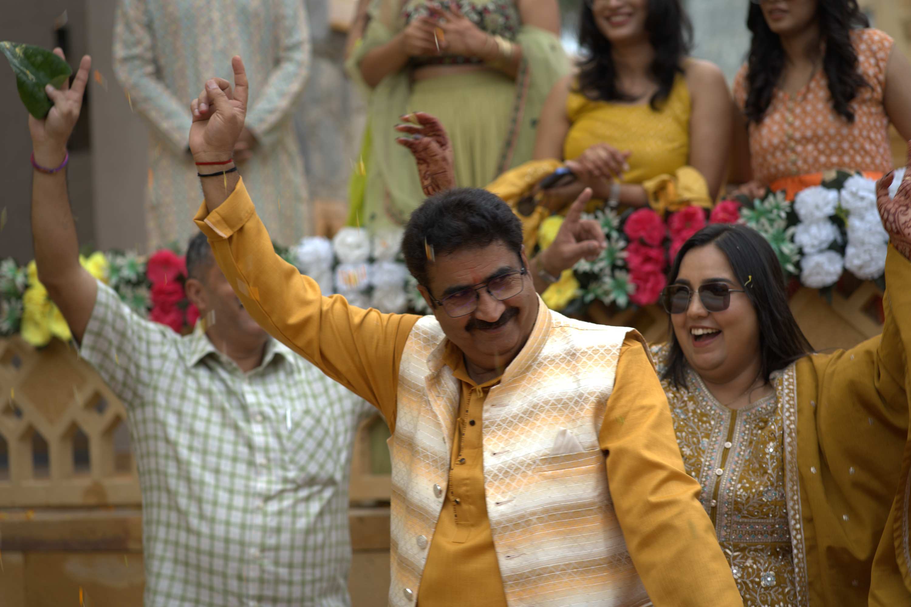 Guests in yellow with their arms up at the haldi